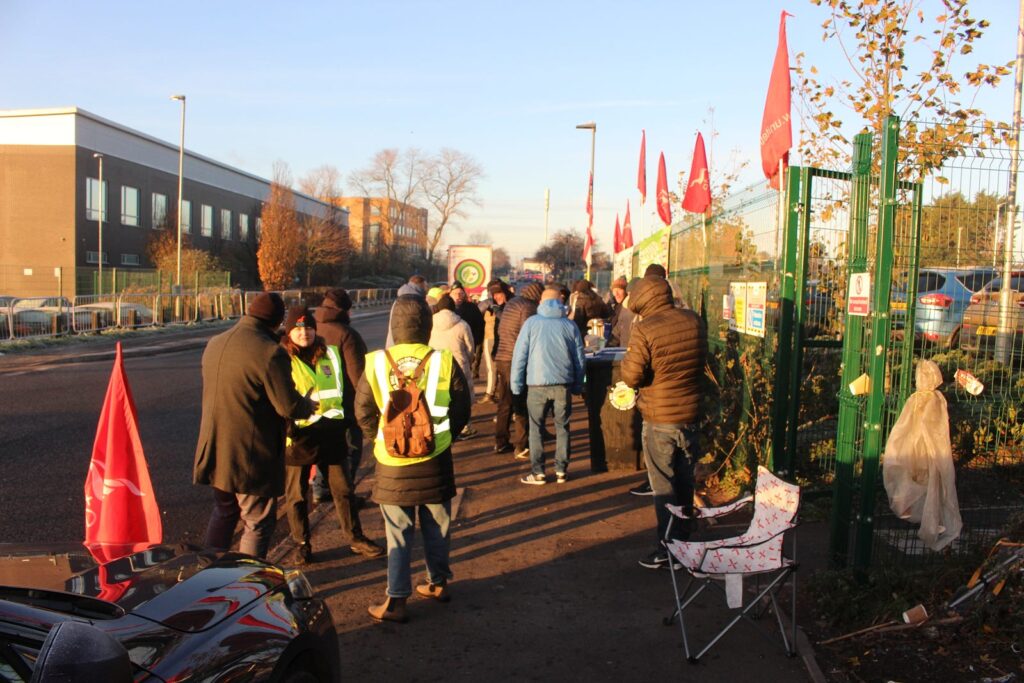 Workers on the Perry Barr picket face away from the camera, watching a lorry driven by agency staff driving down the road, away from the depot.
