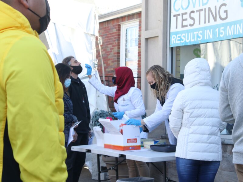 Medical professionals administer rapid tests at an outdoor testing location.